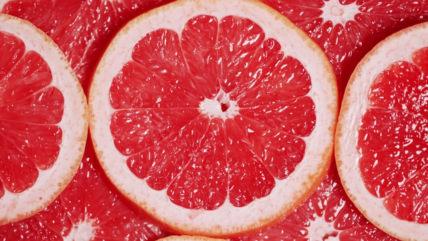 Slow motion of rotation ripe sliced grapefruites. Circles of fresh citrus as food background. Tropical fruits. Concept of proper nutrition or healthy lifestyle. Macro shot.