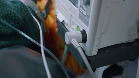 Tilt up view of unrecognizable medical practitioner inserting plug into socket of life support machine and turning switch while taking care of patient in ambulance during emergency.