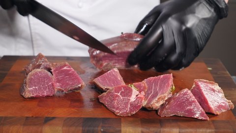 Chef in black gloves cuts raw meat with knife on wooden cutting board. Beef or veal meat on Table before cooking. Butcher in gloves cuts meat into pieces. Raw meat being cut with sharp knife. 4 k
