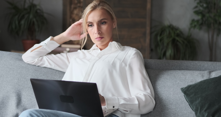 Wistful freelancer woman in white shirt reading online information e learning distance education working remotely. Confident beautiful lady surfing internet chatting use laptop sitting on couch Royalty-Free Stock Footage #1084902730