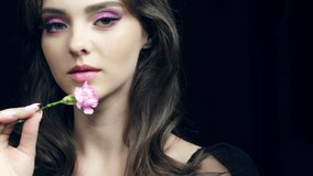 Closeup slow motion video of female with pink carnation flower near lips. Woman with natural lips beauty makeup.