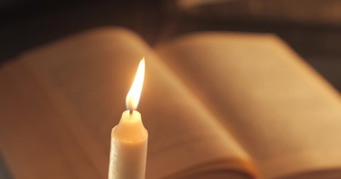 A Burning Candle and an Old Book. Reading and teaching by candlelight at night.
