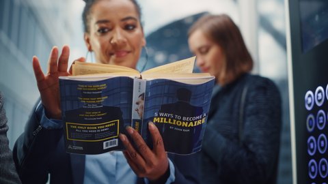 Confident Black Adult Female Riding Glass Elevator to Office in Modern Business Center. African American Manager Reading a Finance Book Called "5 Ways to Become Millionaire" in a Lift.