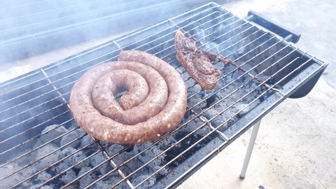 Close up of a long sausage being grilled on a small mobile grill outside for a family feast