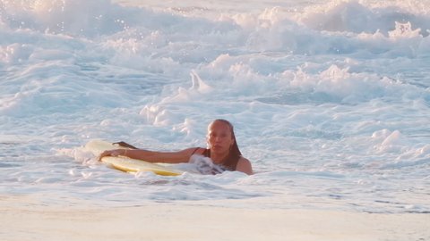 Ocean wave breaks with spray and reveals woman surfer in the water after her Eskimo Roll with yellow surf board