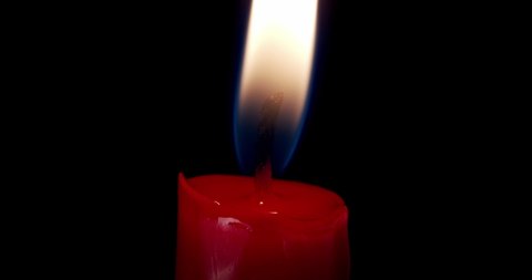 A single red candle burning.Isolated candle burning with dark background.White paraffin candle with yellow shades burns on a black background.Background or illustration of remembrance or celebration