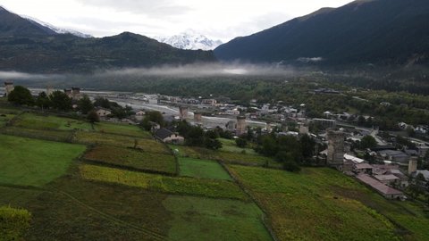 Aerial view on Mestia, Svaneti, Georgia. Cloudy summer day, snowy peaks of the mountain range. Historic heritage of Svan towers and residential houses.