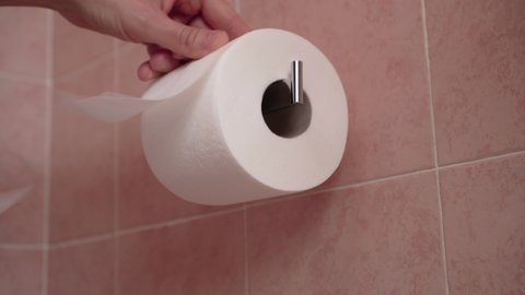 Close up of hands taking toilet paper from a wall mounted toilet roll dispenser.