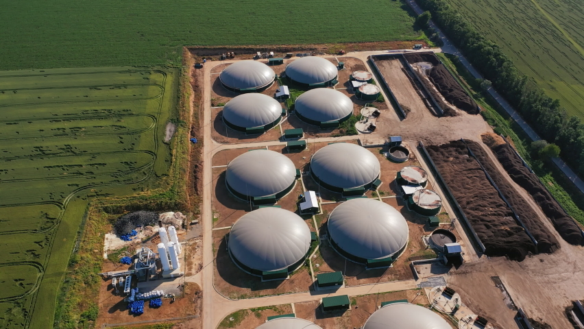 Grey round tops of fuel reservoirs of biogas plant. Organic production of safe energy. Aerial view. Green fields at the backdrop. Royalty-Free Stock Footage #1084925959