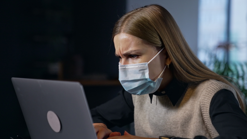 Female worker in protective mask looks disturbed at her laptop. Woman closes computer, takes off her mask and smiles into camera. Royalty-Free Stock Footage #1084926019