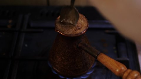 The process of making espresso in a copper pot with long handle and without lid on the gas stove. Male hand with spoon stir hot drink in cezve, foam coffee puts out flame.