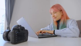 Professional photographer woman with dyed hair networking with clients on internet. White female freelancer typing text on laptop computer. Young girl communicating with clients online in 4k video