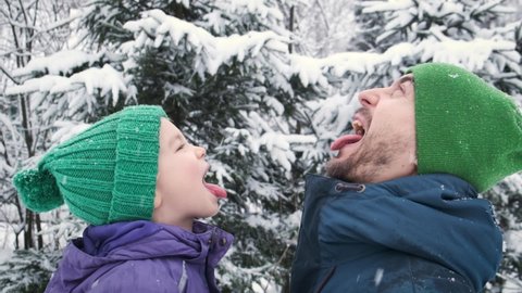 Father and son catching snowflakes by mouth outdoor. Child and dad on snowing winter weather. Positive emotion, kid expression, happy childhood.