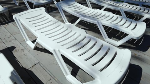Empty deckchair near swimming pool. Plastic beach chair. No people at vacation. Staycation concept. Moving slow motion video. Relax resort spa sitting. Wooden floor