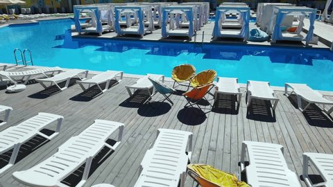 Empty deckchair near swimming pool. Plastic beach chair. No people at vacation. Staycation concept. Moving slow motion video. Relax resort spa sitting. Wooden floor