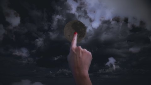Finger Touch Full Moon Turn On Moonlight. Female finger touches the dark moon to turn light on in a cloudy sky at night