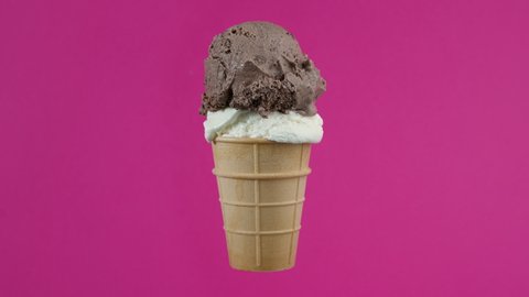 Tasty chocolate and vanilla ice cream balls in waffle cone on pink background. Rotating soft cream, gelato icecream scoop in waffle cone over colorful background