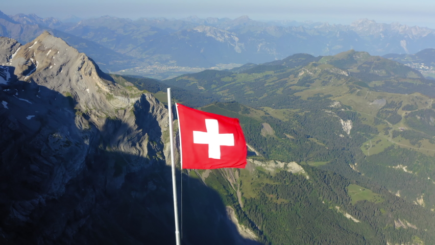 Aerial Descending Panning Red Flag Of Switzerland On Mountain Top, Drone Flying During Winter Season - Vaud, Switzerland Royalty-Free Stock Footage #1084937020