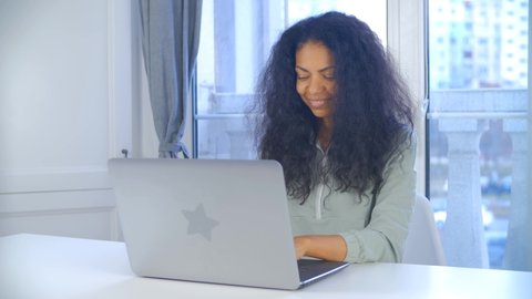 Focused young black woman working on computer. Professional freelancer female typing on laptop keyboard at home on lockdown. African person doing distant free lance work online with smile in 4k video