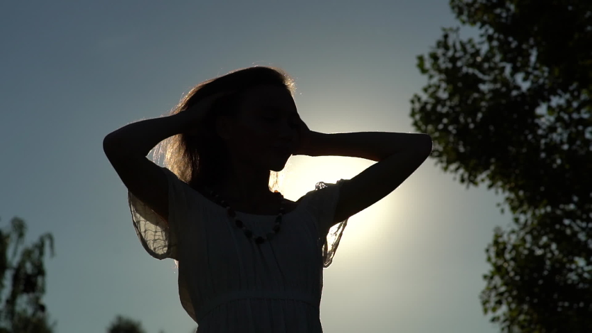 Beautiful woman is spinning, dancing happily in the park. Golden light. White dress. Green environment. Freedom 