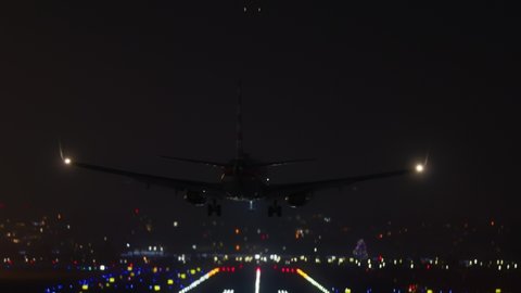 Plane with additional lighting landing over the night city. Single runway airport illuminated at night with cityscape behind. High quality 4k footage