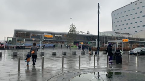 Eindhoven, North Brabant, Netherlands- December 24, 2021: People walk in front of the Eindhoven airport. Front facade and main entrance. Passengers with luggage. Departure, arrival terminals. Fountain