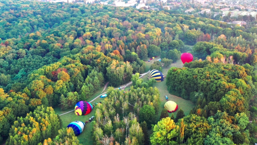 Nice top view of the park, forest covered with greenery. Morning river in fog. Small houses in the background. The balloon is being prepared for flight.