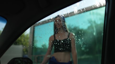 Female hand cleaning car side window with cloth in slow motion. Shooting from inside automobile young slim Caucasian woman washing vehicle at car wash service outdoors