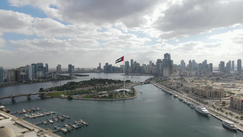 4K-60FPS - Aerial view of the Flag of the United Arab Emirates waving in the air on a cloudy afternoon, The national symbol of UAE over Sharjah's Flag Island, United Arab Emirates, 4K Video Royalty-Free Stock Footage #1084946188