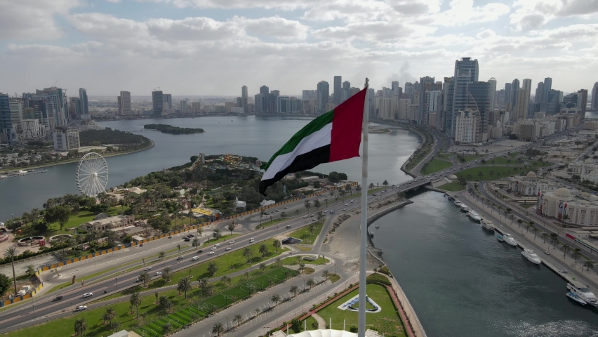 4K-60FPS - Drone view of the Flag of the UAE waving in the air on a cloudy day, The national symbol of UAE over Sharjah's Flag Island, United Arab Emirates, 4K Video Royalty-Free Stock Footage #1084947199