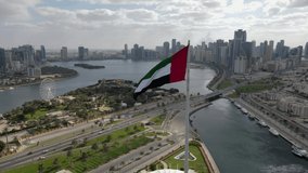 4K-60FPS - Drone view of the Flag of the UAE waving in the air on a cloudy day, The national symbol of UAE over Sharjah's Flag Island, United Arab Emirates, 4K Video