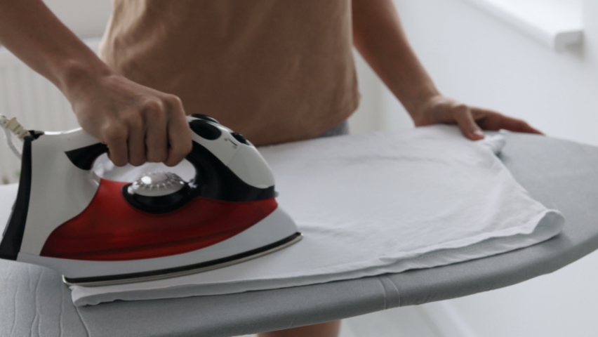 Female hands ironing white clothes with iron on ironing board.  | Shutterstock HD Video #1084947430
