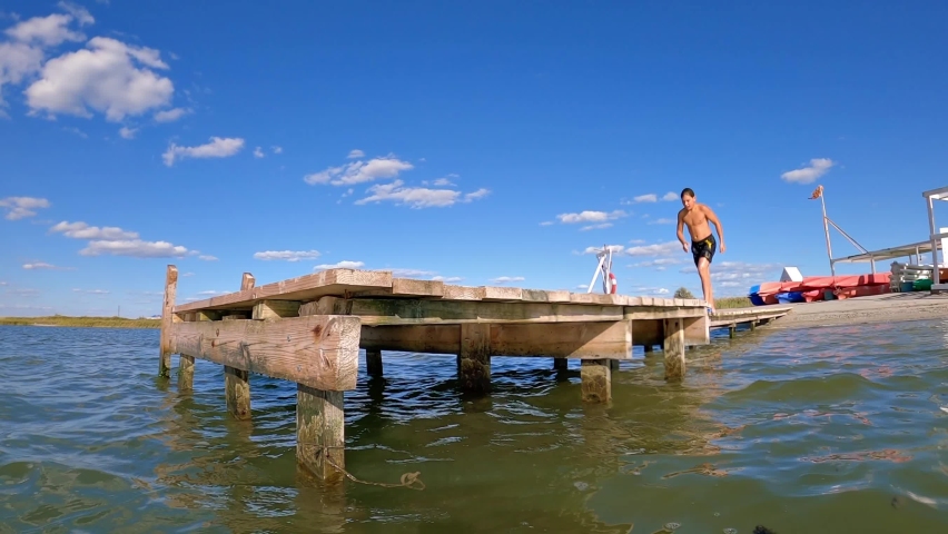The boy runs up and jumps into the water, lake, river, sea. Wooden pier. Slow motion. Nice flip.