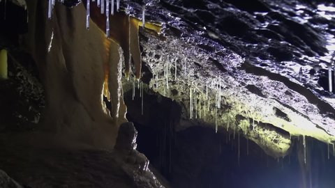 Yellow stalactite drips water onto stalagmite below in deep dark cave
