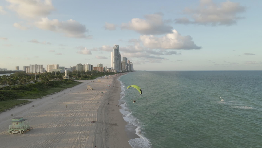 Aerial follows acrobatic paramotor flight over Haulover Beach, Miami