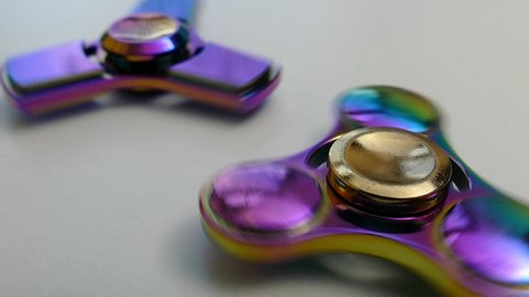 Two iridescent fidget spinners spinning on a white surface, roller toy for kids, object for anxiety