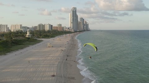 Motorized paraglider flies low over sandy Miami Beach in afternoon sun