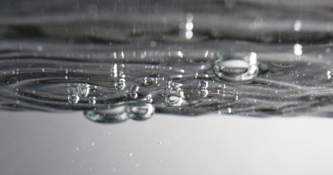 Close Up Lockdown Shot Of Water Surface With Bubbles Rising And Forming As Liquid Is Added Against White Background