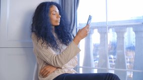 Happy young adult black woman using smartphone. Attractive African female browsing internet on modern mobile phone device at home. Smiling person reading social media news feed on cellphone i 4k video
