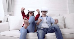 Couple wearing virtual reality glasses headsets playing VR video games in the living room together.