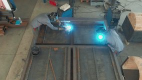 Two welders in protective masks works with metal steel and iron using a welding machine, bright sparks and flashes. Work in the shop. Video from above. 4k