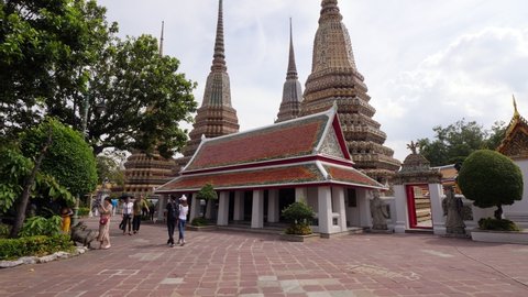 BANGKOK - MAY 07, 2018: Pavilion building in traditional Thai style and ornate Chedi towers at courtyard of Wat Pho, camera tilt up, show thin spires of stupa-like buildings. Few unidentified people