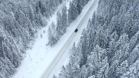 Black car driving on the snow road. Drone view, winter time. Trees in the snow.
