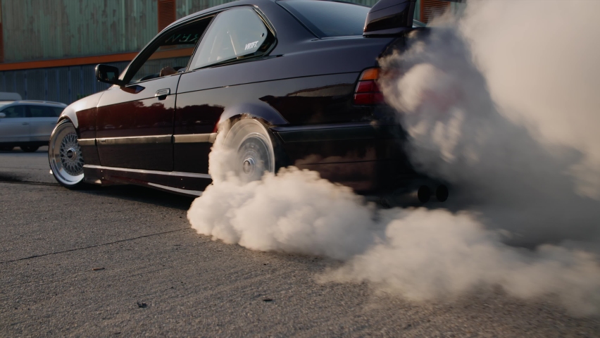 A black shiny car with tuning adjustments drifts in place and creates smoke from the tires Royalty-Free Stock Footage #1084977097