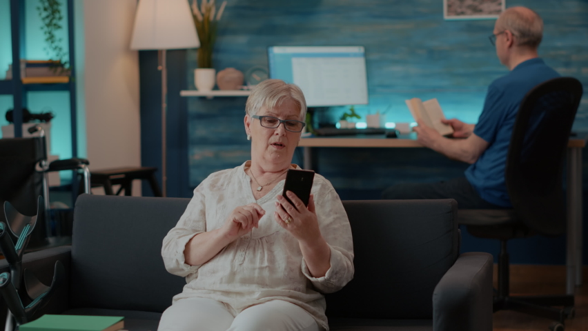 Senior woman chatting on remote video call in living room. Old adult using mobile phone to have conversation on online videoconference for telecommunication. Internet meeting on smartphone Royalty-Free Stock Footage #1084977313