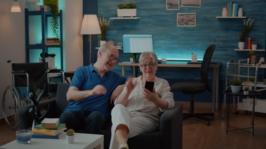Senior couple talking to relatives on online video call at home, using smartphone to chat. Retired people with chronic disability holding phone to have remote conversation on teleconference. Royalty-Free Stock Footage #1084977514
