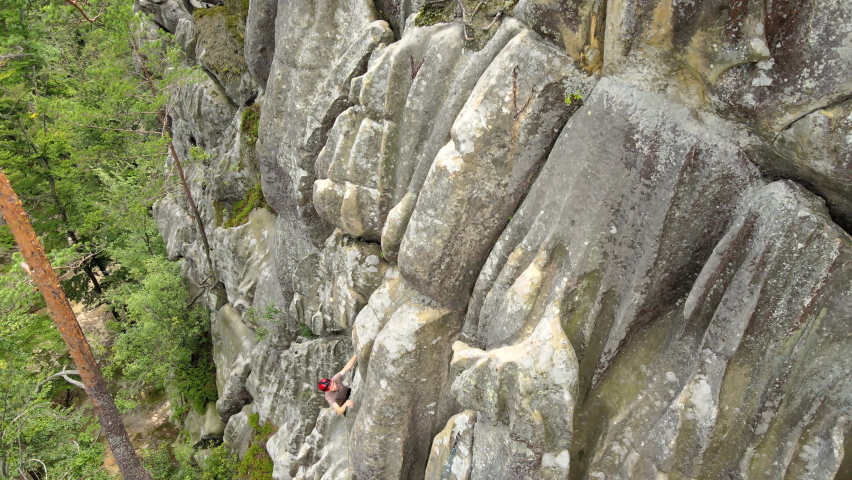 Strong male climber climbing steep wall of rocky mountain. Sportsman overcoming difficult route. Engaging in extreme sports hobby concept