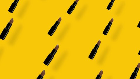 Colorful pattern of lipsticks on yellow background with shadows. Seamless pattern with lipstick. Top view. Realistic animation. 4K video motion