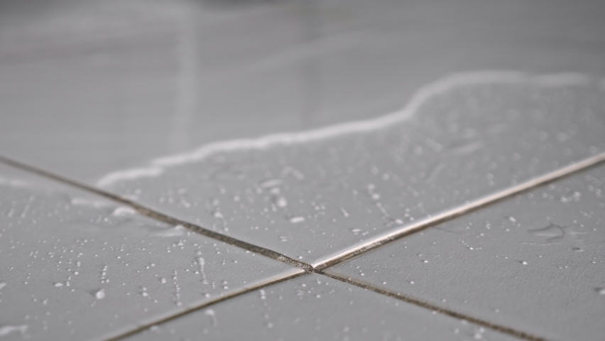 Clean water flows on floor covering white ceramic tile because of hard pipe damage causing flood in apartment bathroom close view. | Shutterstock HD Video #1084982356