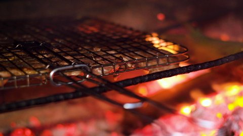Lamb chops in grid sizzling on smoky open coal fire; barbecue outside